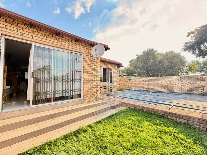 Rear garden area featuring a swimming pool with cover, tiled patio steps leading to the house, and a brick boundary wall.