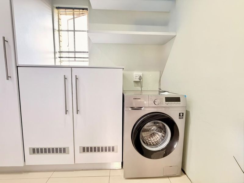 A functional laundry area featuring white built-in cabinetry, floating storage shelves, and tiled flooring with a dedicated space for a washing machine.