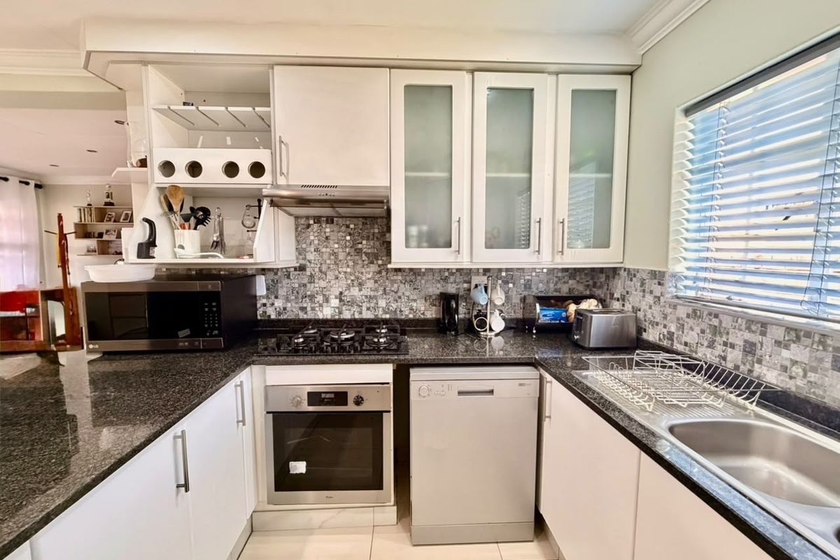 A functional kitchen featuring granite countertops, a gas hob, built-in oven, extractor fan, and mosaic tile backsplash with ample cabinetry.
