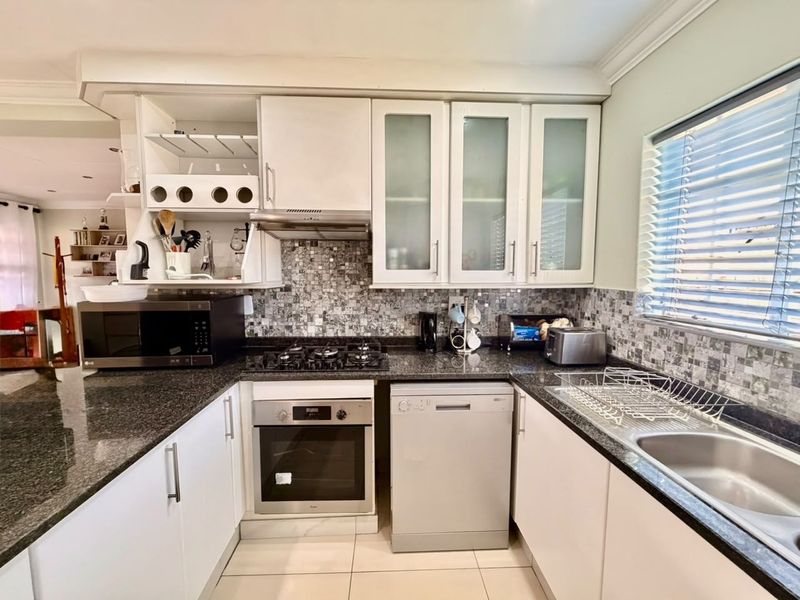 A functional kitchen featuring granite countertops, a gas hob, built-in oven, extractor fan, and mosaic tile backsplash with ample cabinetry.
