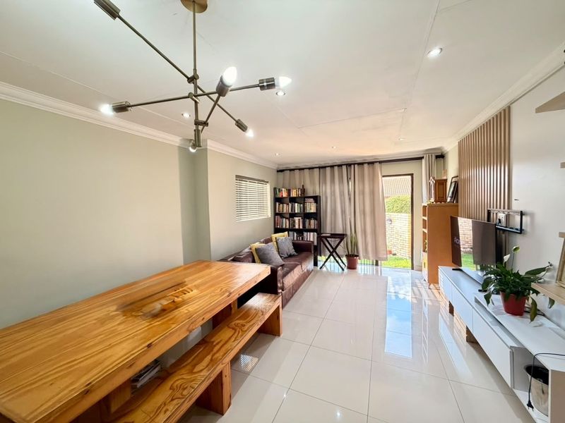 Bright open-plan living and dining area featuring polished porcelain tiles, a contemporary feature wall, and direct access to the outdoor space.