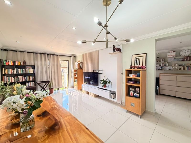 Spacious living room featuring polished tiled flooring, a modern chandelier, and a custom built-in media unit with direct access to the outdoor area.