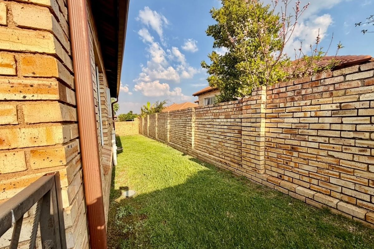 A side garden area featuring a well-maintained lawn, enclosed by a sturdy face brick boundary wall and the side elevation of the house.