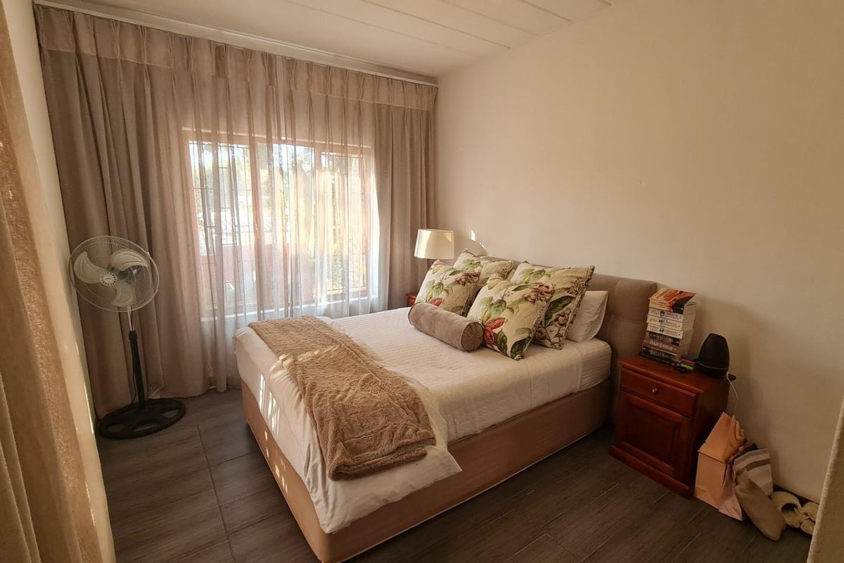 A cozy bedroom featuring tiled flooring and large windows with curtain tracks, providing natural light and a view through security bars.
