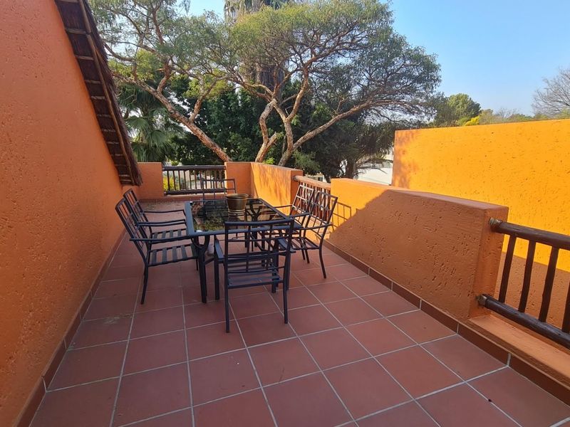 A spacious outdoor balcony featuring tiled flooring, textured plaster walls, and a timber balustrade, offering an open-air space for relaxation.