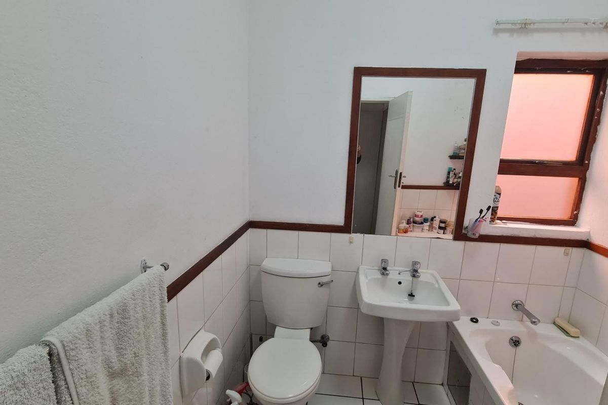 A functional bathroom featuring a pedestal washbasin, toilet, and bathtub with tiled splashbacks and a wall-mounted mirror.