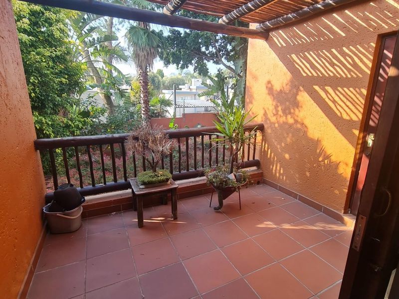 A covered balcony featuring terracotta tiled flooring, a wooden balustrade, and a rustic timber pergola, offering an outdoor space with garden views.