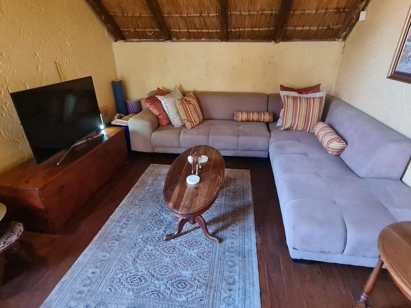 Cozy living room featuring a rustic thatched roof with exposed timber rafters, textured walls, and warm timber flooring.