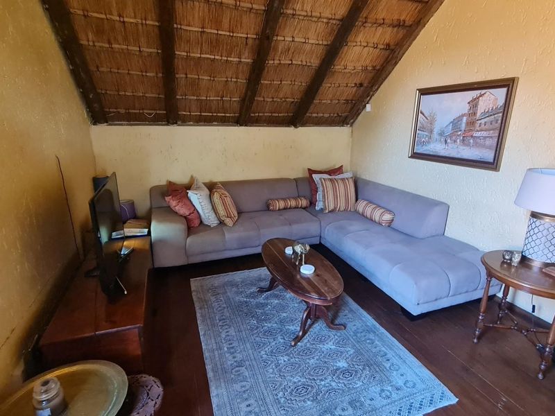 A cozy living room featuring a unique thatched ceiling with exposed timber rafters, textured walls, and warm timber flooring.