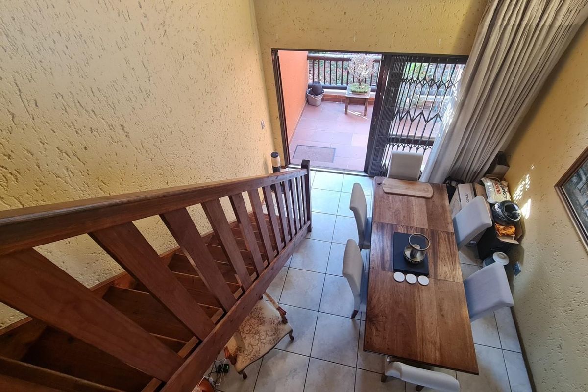 A high-angle view of a living area featuring a wooden staircase, tiled floors, and direct access to an outdoor balcony through sliding glass doors.