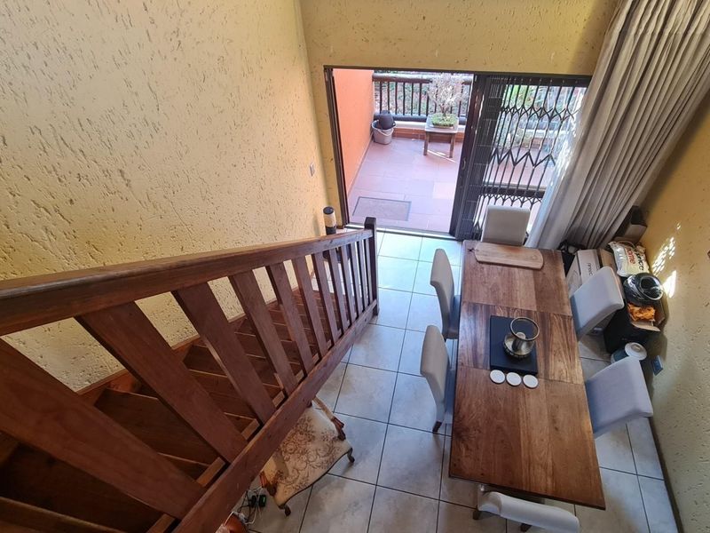 A high-angle view of a living area featuring a wooden staircase, tiled floors, and direct access to an outdoor balcony through sliding glass doors.