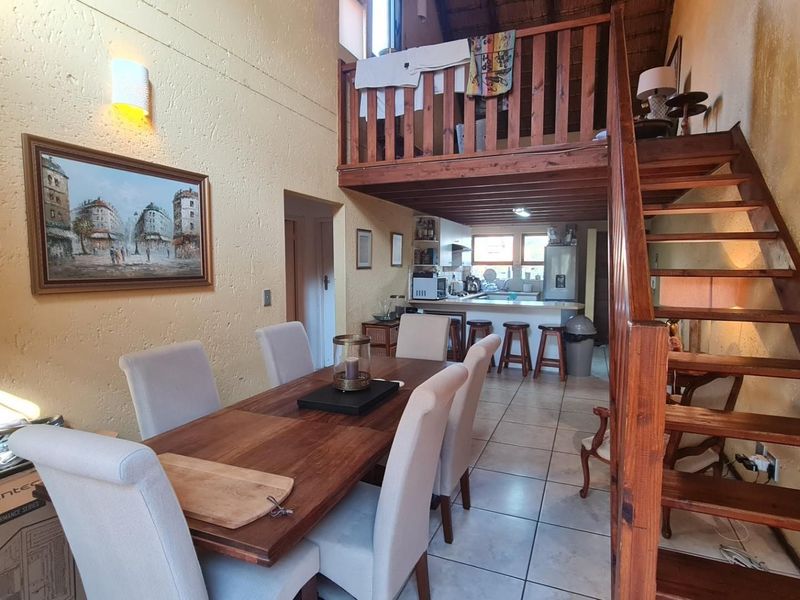 Open plan living and dining area featuring a wooden mezzanine loft, staircase, and a functional kitchen with a breakfast bar.