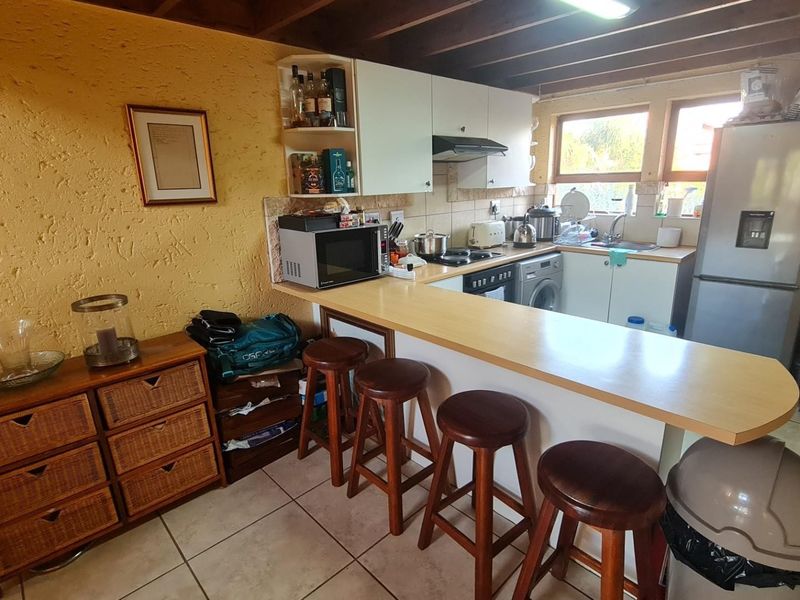 A functional kitchen featuring a breakfast bar, built-in cabinetry, integrated appliances, and exposed timber ceiling beams, offering a practical layout for daily use.