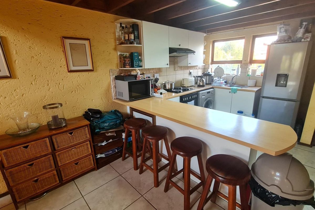 A functional kitchen featuring a breakfast bar, built-in cabinetry, integrated appliances, and exposed timber ceiling beams, offering a practical layout for daily use.