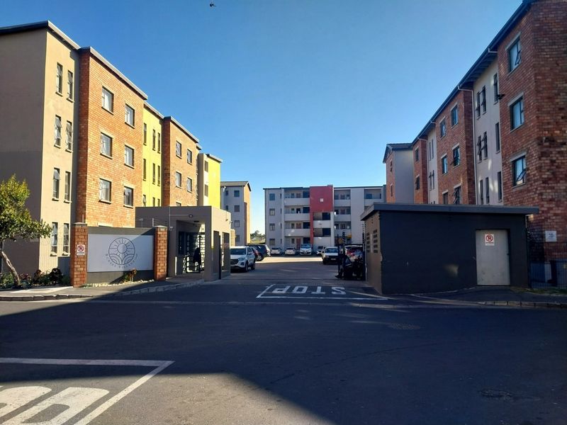 Front entrance view of the apartment complex featuring brick and rendered facades, secure gated access, and paved driveway.