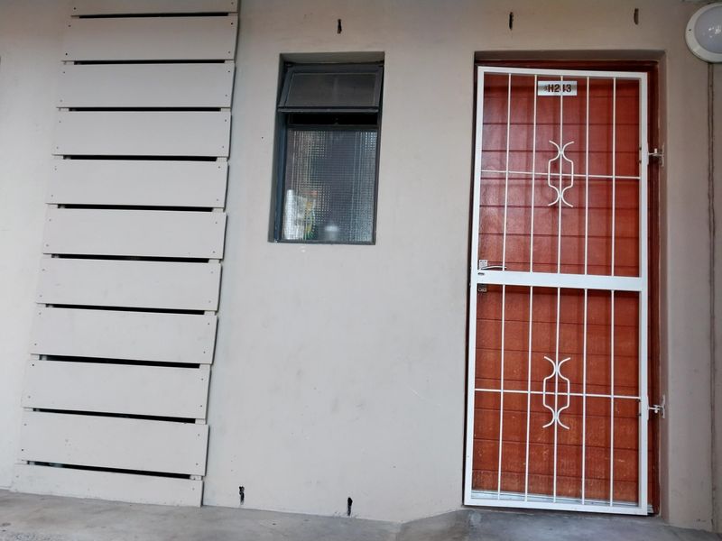 Front entrance of the apartment featuring a timber door with a white security gate, a top-hung window, and decorative wall cladding.