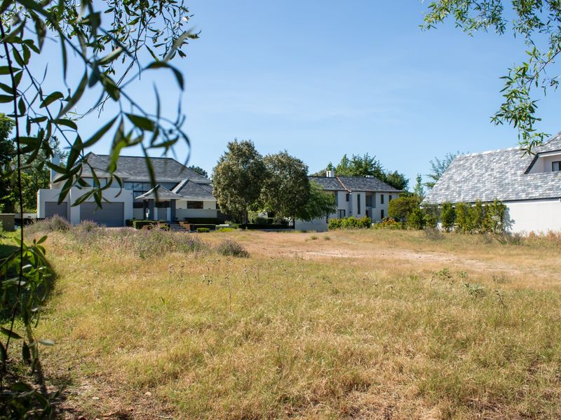 A view of a vacant residential plot of land with surrounding established residential properties in the background.