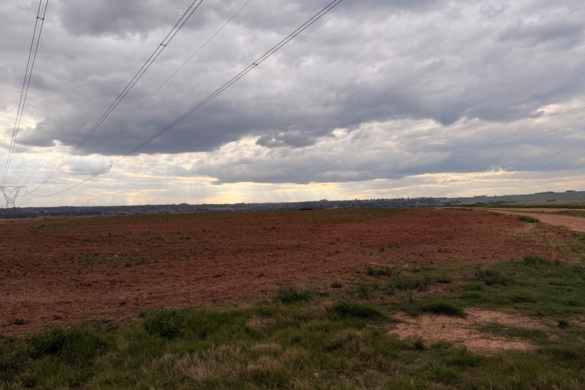 Expansive view of open farmland with a dirt road and overhead power lines under a cloudy sky.