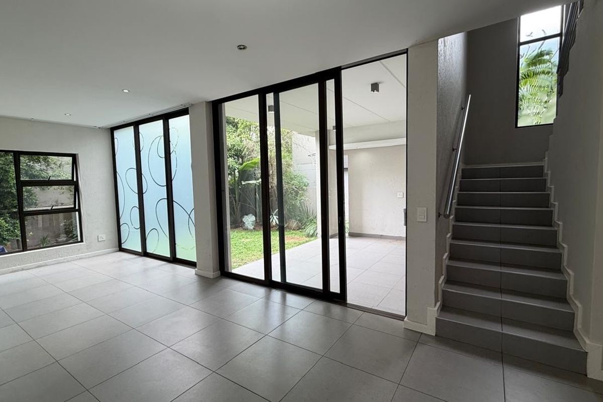 Spacious open-plan living area featuring large sliding glass doors leading to a patio, tiled flooring, and a modern staircase with a metal handrail.