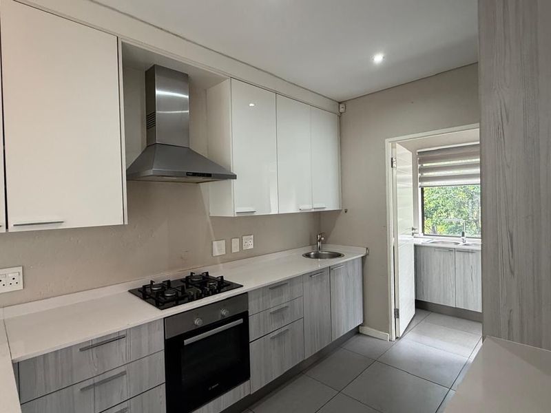 Modern kitchen featuring white and wood-grain cabinetry, stone countertops, gas hob, built-in oven, and an adjoining scullery area with additional sink and storage.