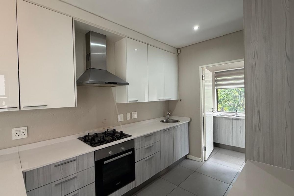 Modern kitchen featuring white and wood-grain cabinetry, stone countertops, gas hob, built-in oven, and an adjoining scullery area with additional sink and storage.
