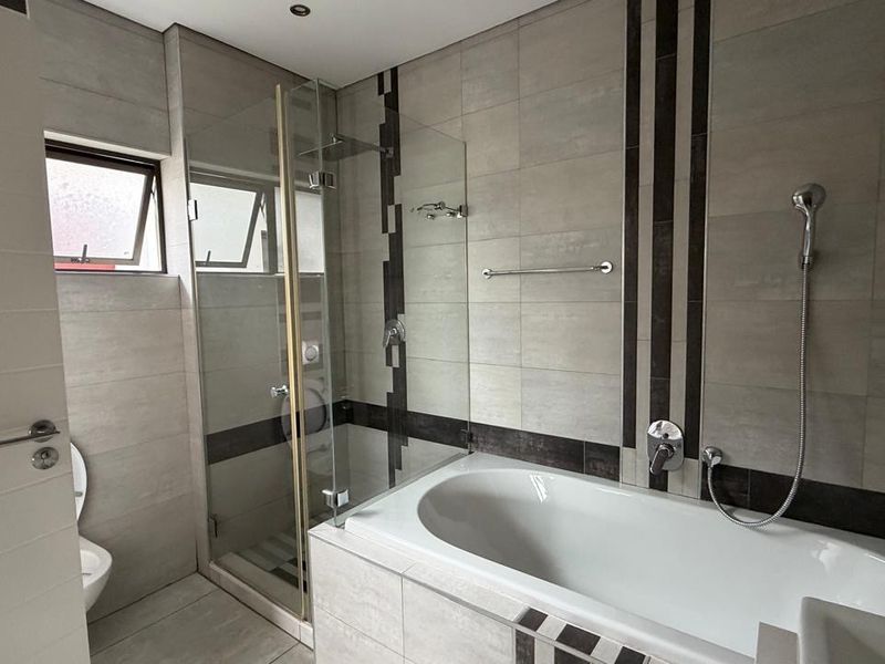 Modern bathroom featuring a built-in bathtub, separate glass-enclosed shower, and neutral tiled finishes throughout.