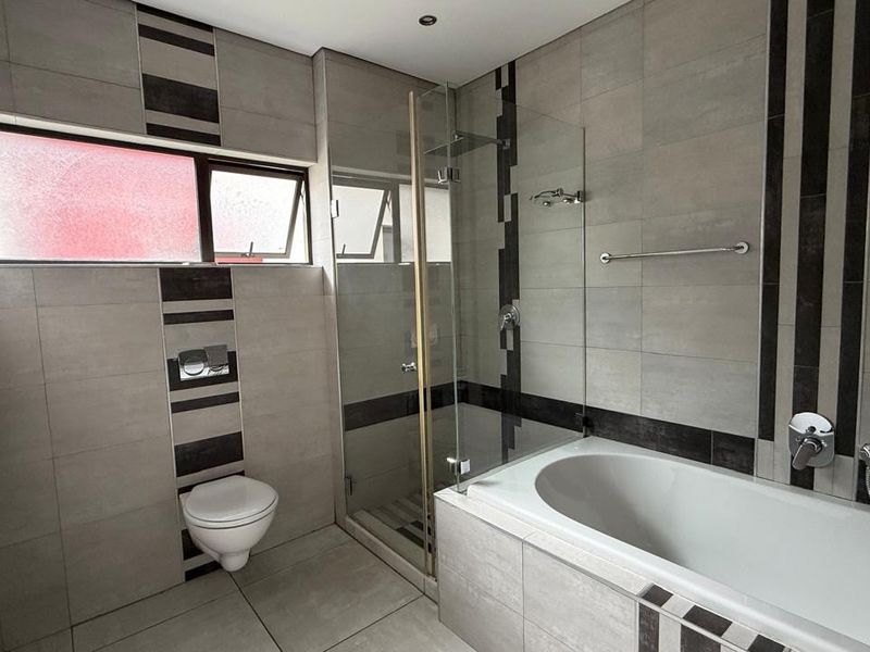 Modern bathroom featuring a wall-hung toilet, glass-enclosed shower, and a built-in bathtub with contemporary tiled finishes.