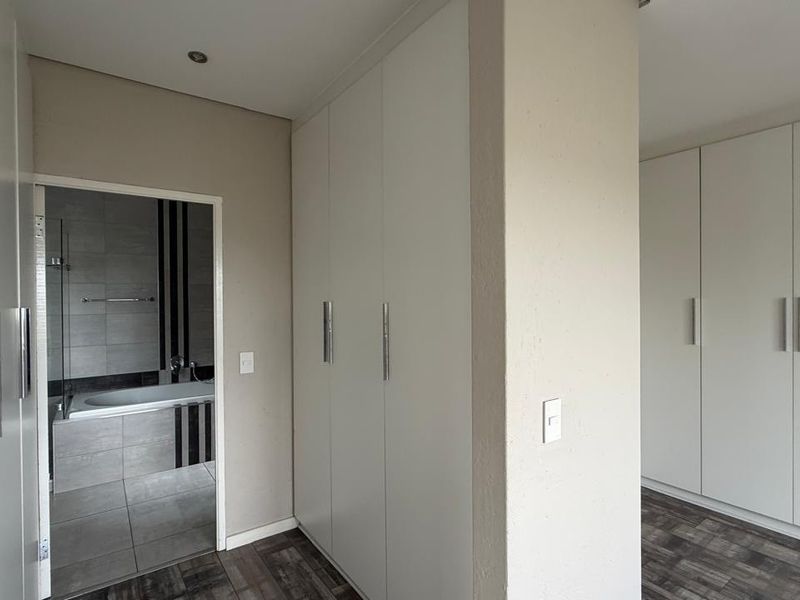 A spacious bedroom area featuring extensive built-in cupboards, modern laminate flooring, and direct access to an en-suite bathroom with contemporary tiling.