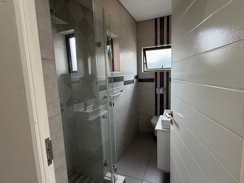A modern, compact bathroom featuring a glass-enclosed shower, wall-mounted toilet, and a sleek vanity basin with contemporary tiled finishes.