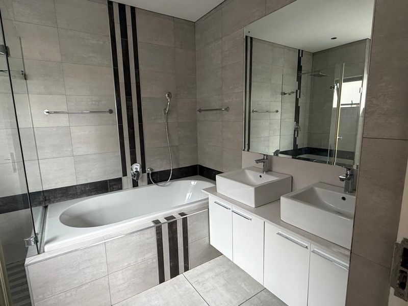 Modern bathroom featuring a double vanity, built-in bathtub, and a separate glass-enclosed shower with contemporary grey tiling throughout.