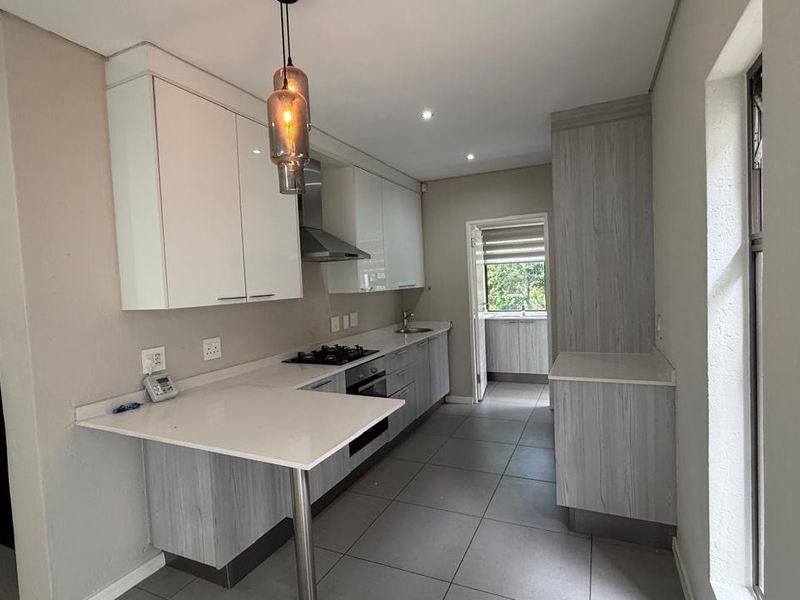 Modern kitchen featuring sleek white and wood-grain cabinetry, stone countertops, gas hob, and tiled flooring, offering a clean and functional workspace.