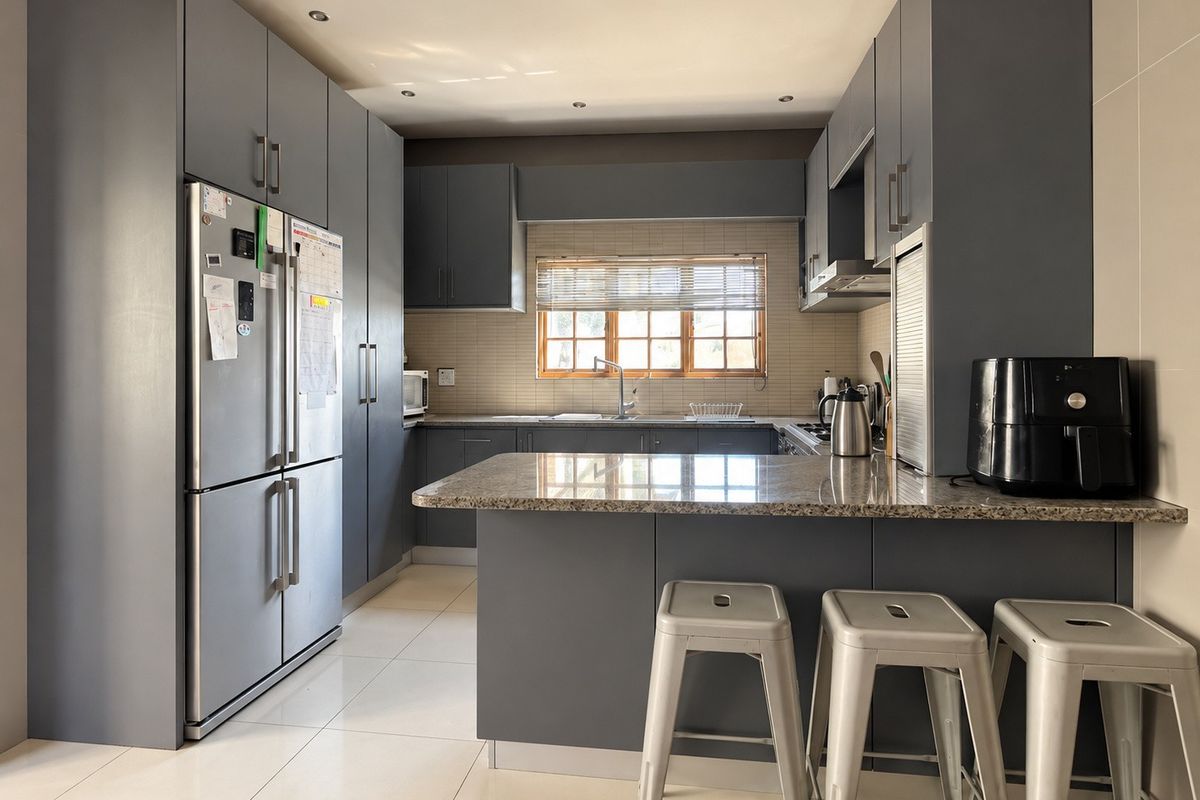 Modern kitchen featuring sleek grey cabinetry, granite countertops, a breakfast bar, and tiled flooring with integrated lighting.