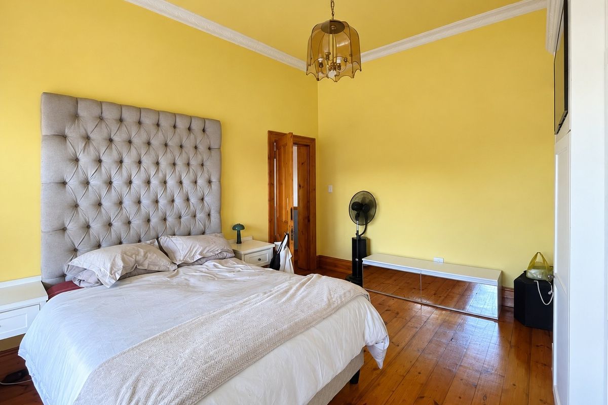 Spacious bedroom featuring original hardwood flooring, decorative crown molding, and a classic timber door frame, offering a bright and traditional aesthetic.