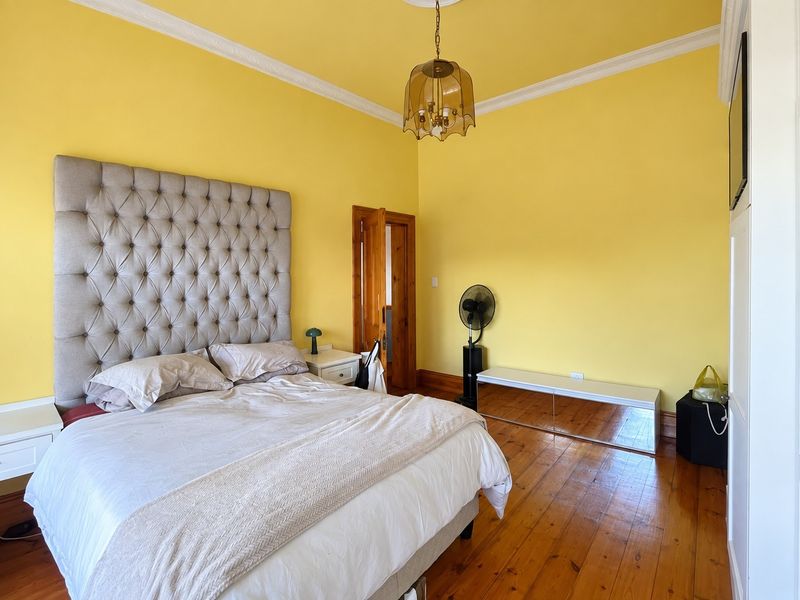 Spacious bedroom featuring original hardwood flooring, decorative crown molding, and a classic timber door frame, offering a bright and traditional aesthetic.