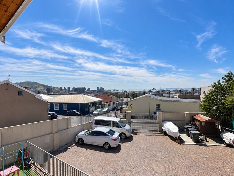 An elevated view of the rear paved driveway and parking area, featuring perimeter walling, security gates, and a distant cityscape view.