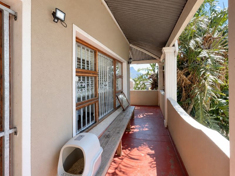 A covered balcony featuring a painted concrete floor, security bars on windows, and structural columns, offering a functional outdoor space.