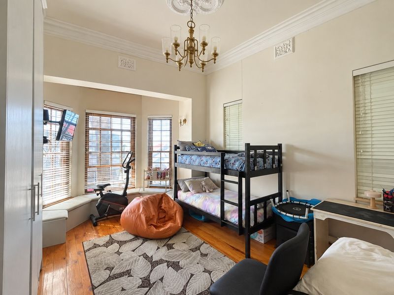 Spacious bedroom featuring polished hardwood flooring, a classic ceiling rose, ornate cornice detailing, and a large bay window with built-in seating.