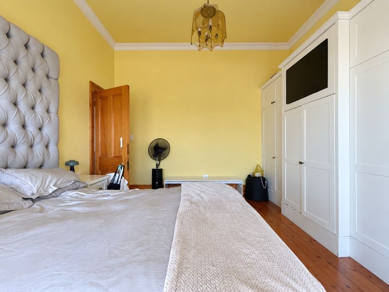 A bedroom featuring timber flooring, crown molding, and a large built-in wardrobe with integrated television space.