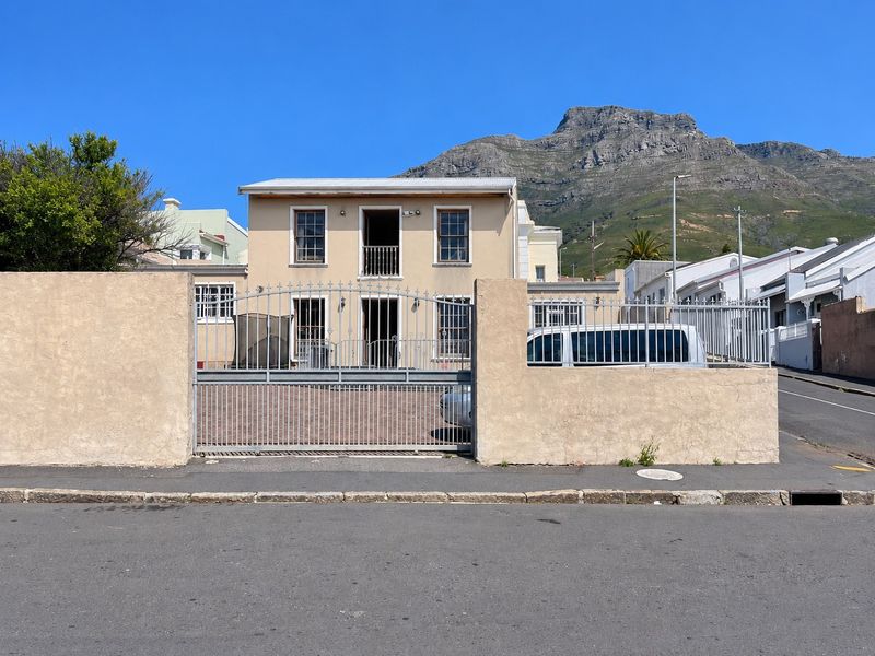 Front elevation of a two-story house featuring a secure metal gate, paved driveway, and mountain views in a residential setting.