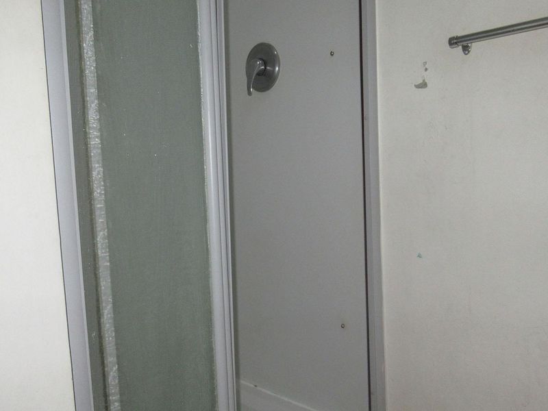 A compact bathroom featuring a shower enclosure with a mixer and a wall-mounted towel rail, showing signs of wear on the wall finish.