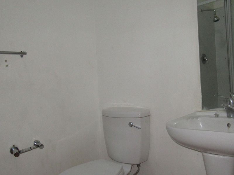 A functional bathroom featuring a pedestal basin, toilet, and shower enclosure, requiring cosmetic updates to improve its overall condition and appeal.