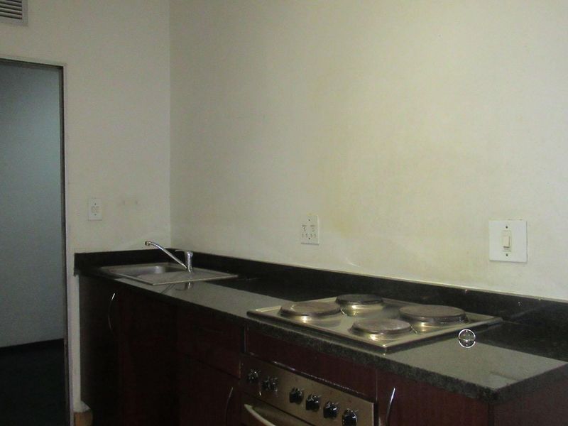 A compact kitchen featuring dark wood cabinetry, granite countertops, a built-in oven and hob, and a stainless steel sink.