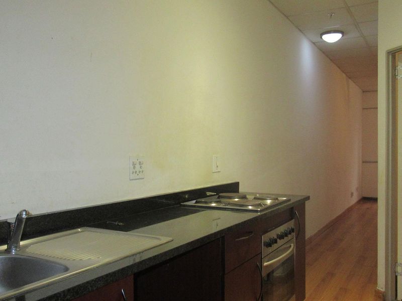 A compact kitchenette featuring a built-in oven, hob, granite countertops, and a stainless steel sink, set within a minimalist, empty apartment space.