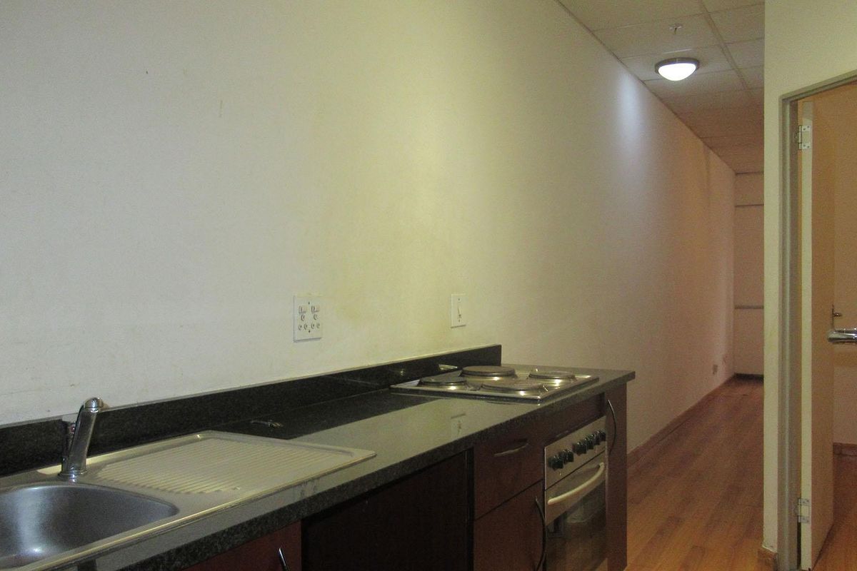 A compact kitchenette featuring a built-in oven, hob, granite countertops, and a stainless steel sink, set within a minimalist, empty apartment space.