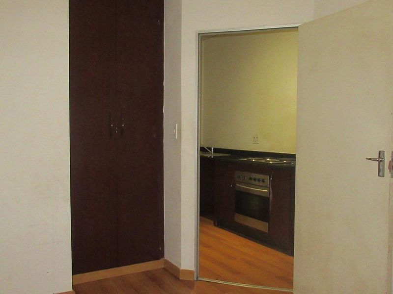 A bedroom featuring laminate flooring and a built-in wardrobe, with a view into the adjacent kitchen area.