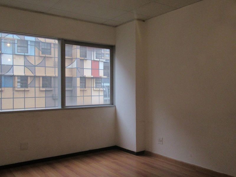 An empty bedroom featuring laminate flooring, a large window with urban views, and neutral walls, offering a blank canvas for personalization.