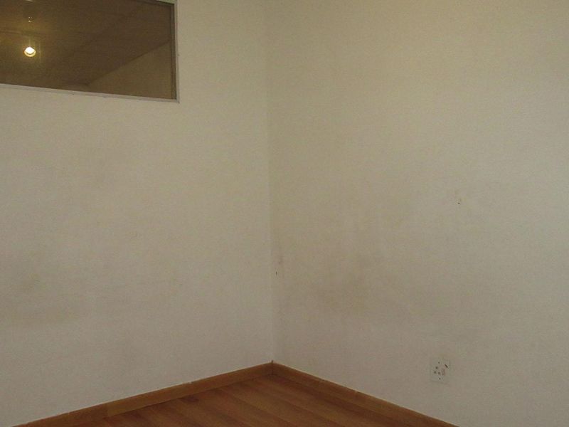 An empty bedroom featuring laminate flooring, a high-level window, and electrical outlets, requiring cosmetic attention to the wall surfaces.