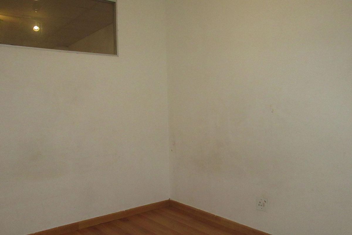 An empty bedroom featuring laminate flooring, a high-level window, and electrical outlets, requiring cosmetic attention to the wall surfaces.