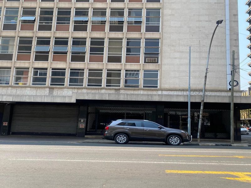 Street-level view of a multi-story apartment building facade featuring metal roller shutters and security razor wire along the lower perimeter.