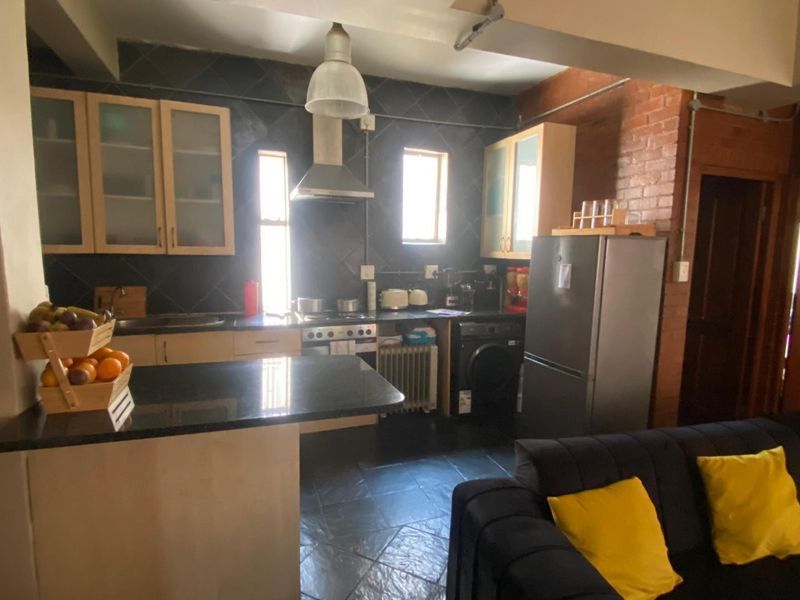 Open-plan kitchen and living area featuring exposed brick walls, slate flooring, dark cabinetry, and a breakfast bar with granite countertops.
